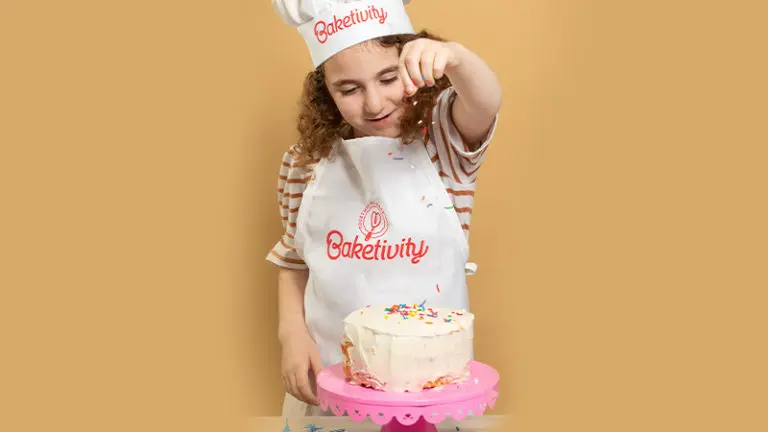 Girl baking birthday cake with Baketivity hat and apron