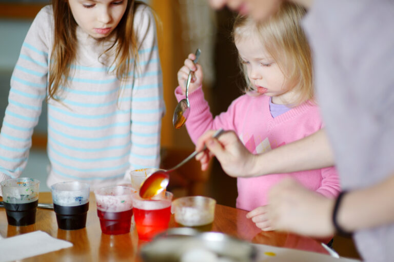 Young mother and her two little daughters painting colorful Easter eggs at home