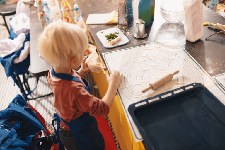 Cooking baking workshop class for school kids. Cute little boy in kitchen apron playful learning to bake cakes having fun. Kids playing with wheat flour and rolling pin