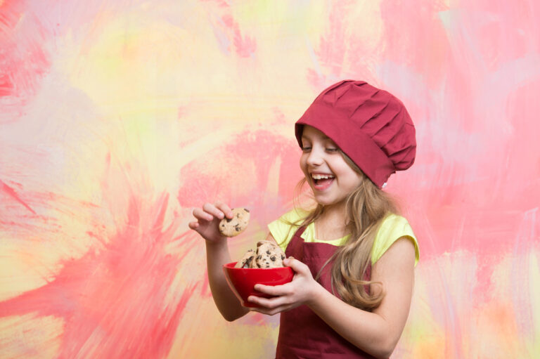 Small happy girl chef in hat, apron with cookies bowl