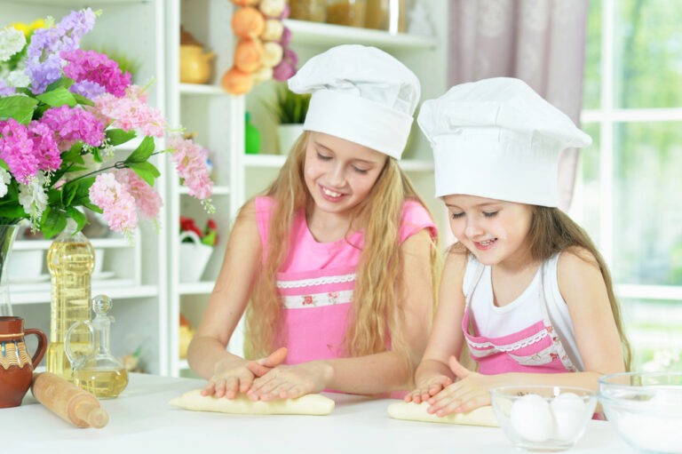 Cute little girls in chefs hats making dough in the kitchen at home