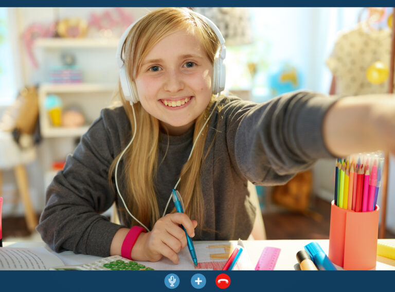 Portrait of smiling modern child with headphones homeschooling, having video conference at home in sunny day.