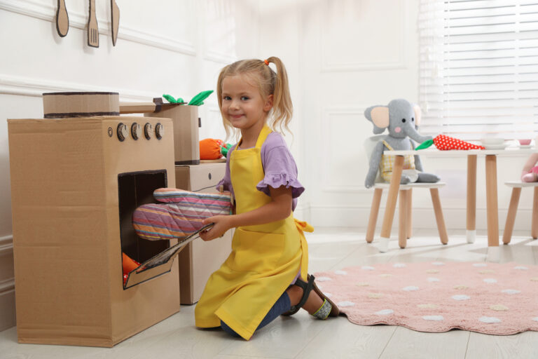 Little girl playing with toy cardboard oven at home